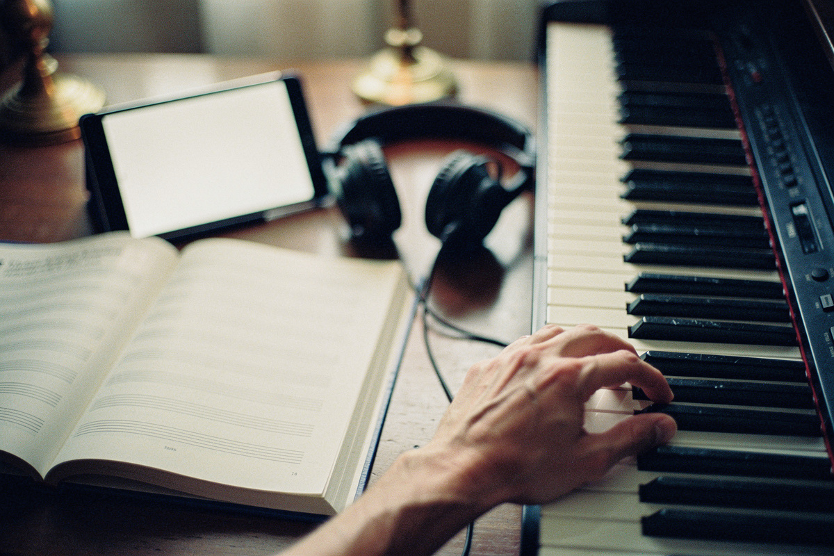 A method book, a tablet and headphones beside a digital piano