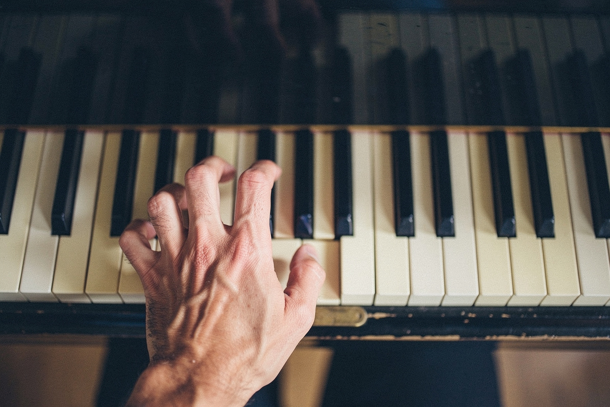 An adult left hand shaping a chord on piano keys